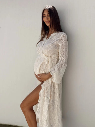 Pregnant woman in a white lace dress against a plain background
